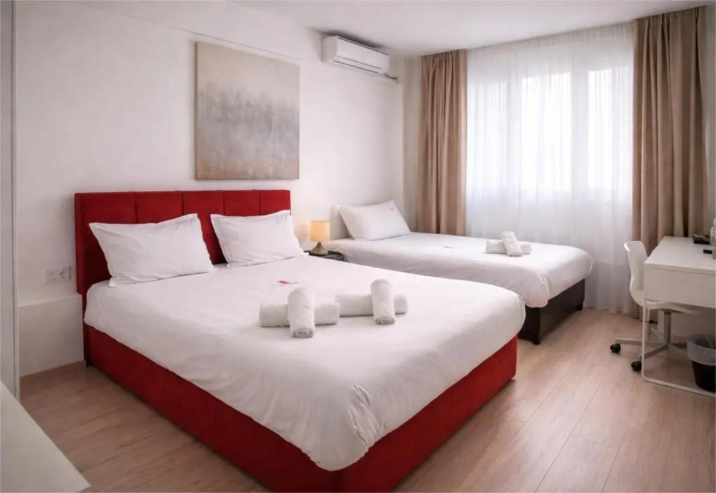 realistic photo of the Triple room of City Plaza hotel featuring one large double bed with red details and a single bed next to it