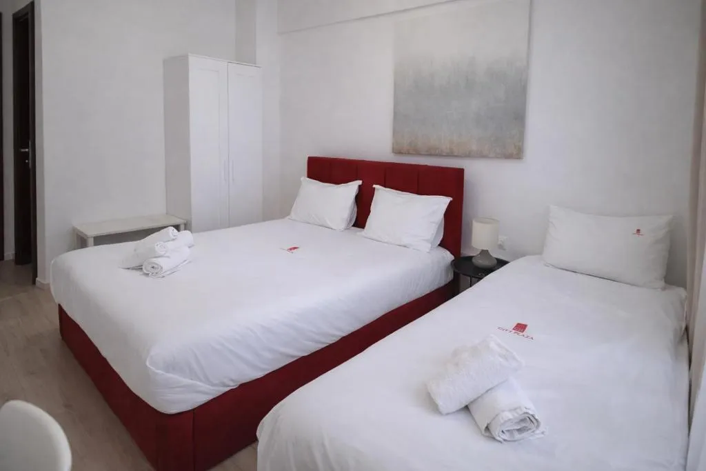 realistic photo of the Triple room of City Plaza hotel featuring one large double bed and a single bed next to it with a modern painting on the wall behind